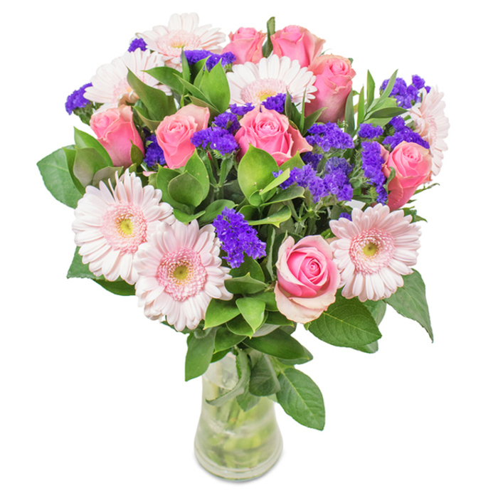 A striking, expertly arranged floral bouquet from a Norbiton florist, displayed in a clear glass vase against a crisp white background. At the heart of the arrangement, approximately seven to nine pink roses form a graceful centrepiece, some petals still tightly furled, others beginning to reveal their classic spiral shape. These roses are complemented by five to seven pale pink Gerbera daisies, their wide, round heads and radiating petals adding joyful volume, each centre a delicate cream almost fading to white. Interwoven among the blush blooms, vibrant clusters of deep purple statice or limonium provide lively contrast, catching the eye and adding texture. The rich, deep green foliage below gives a sense of abundance, evoking the leafy parks that define the Norbiton landscape, while supporting the visual freshness of the composition. The transparent vase, with water glistening around the bundled stems, completes the natural, freshly-delivered look beloved by local residents. This elegant mix of roses, gerberas, and purple accents is ideal for Norbiton celebrations-whether birthday gatherings, anniversaries, Mother's Day surprises, or a tasteful touch for a Raynes Park office. The arrangement embodies affection, joy, and thoughtful celebration, offering a fresh reminder of Norbiton's enduring charm and the artistry of its local florists.